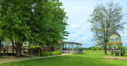 A scenic view of a building with a porch, surrounded by trees, and a sign for Tonitown, Arkansas.