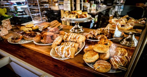 A display of assorted pastries and baked goods, including croissants, scones, and sweet rolls, on a wooden counter.