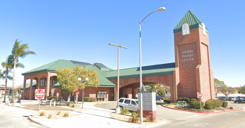 Oxnard Transit Center, a brick building with a green roof, featuring a clock tower and palm trees in the foreground.