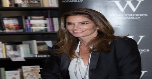 A woman with long brown hair smiles in front of a bookshelf at a bookstore event.