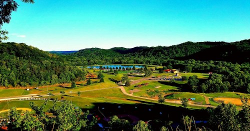 A scenic view of a lush green landscape with a lake, rolling hills, and a clear blue sky.