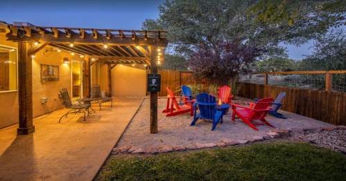 Cozy outdoor seating area with colorful chairs, a fire pit, and string lights under a wooden pergola.