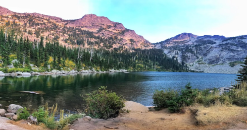 A serene mountain lake surrounded by lush trees and rocky peaks under a clear blue sky.