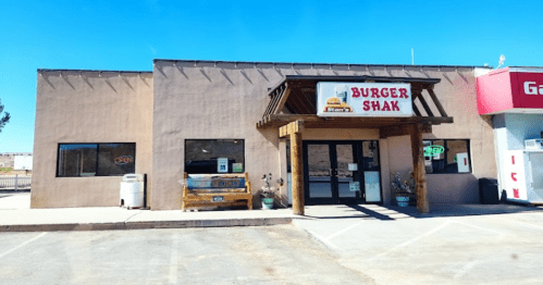Exterior of a restaurant called "Burger Shak," featuring a wooden awning and a parking lot under a clear blue sky.