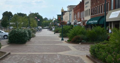 A charming downtown street lined with shops, greenery, and brick pathways under a partly cloudy sky.