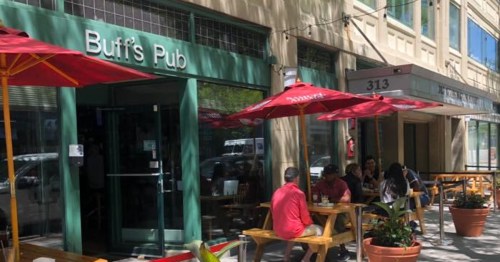 Outdoor seating at Buff's Pub, featuring red umbrellas and patrons enjoying their meals on a sunny day.
