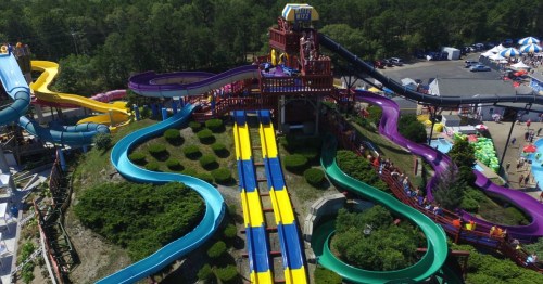 Aerial view of a colorful water park with multiple slides and a large play structure surrounded by greenery.