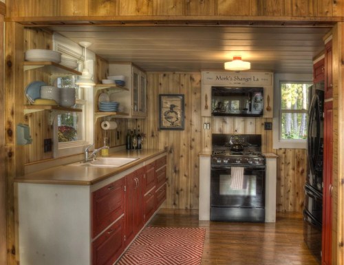 Cozy kitchen with wooden walls, red cabinets, a sink, stove, and decorative plates, creating a warm, inviting atmosphere.