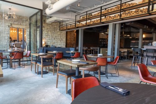Modern restaurant interior featuring wooden tables, red chairs, and a stone wall, with a cozy, inviting atmosphere.