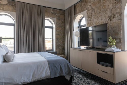 Modern bedroom featuring a bed, stone walls, large windows, a TV, and stylish decor.