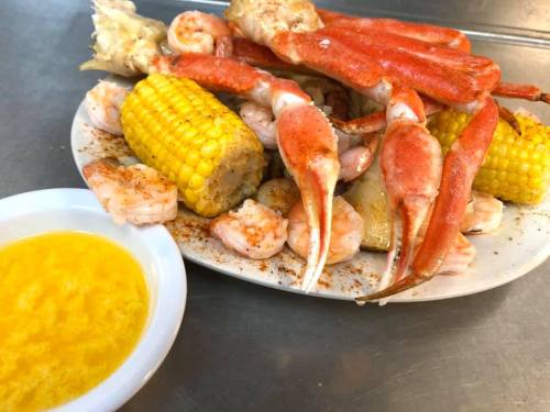 A platter of seafood featuring shrimp, crab legs, corn, and a side of melted butter.