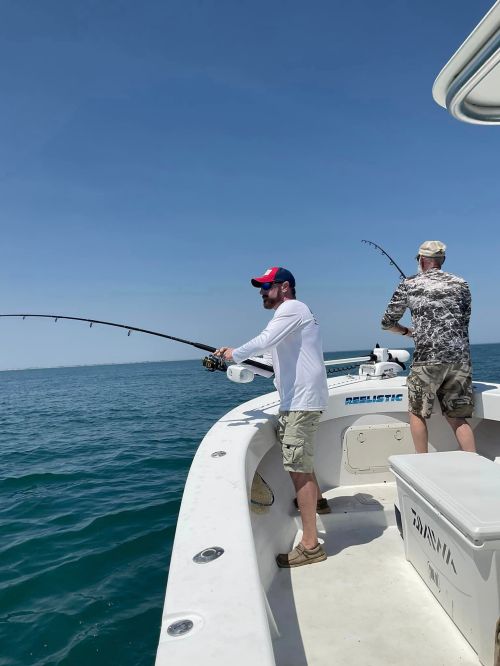 Two men fishing from a boat on a sunny day, casting lines into the calm blue water.