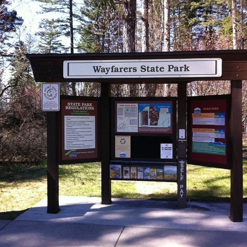 Signage at Wayfarers State Park with park regulations, fees, and a map, surrounded by trees.