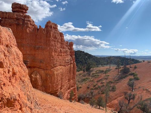 A scenic view of red rock formations and a blue sky with scattered clouds in a mountainous landscape.