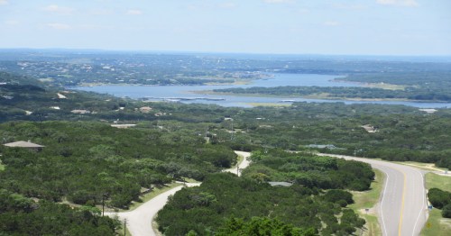 A scenic view of a lush green landscape with winding roads and a large body of water in the distance under a clear blue sky.