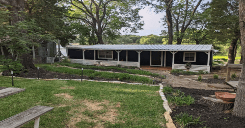 A cozy blue cabin surrounded by greenery, with a stone path and outdoor seating in a serene, natural setting.