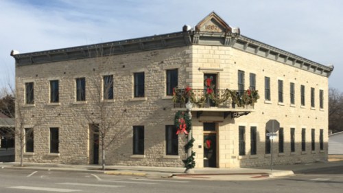 Historic stone building decorated for the holidays, featuring wreaths and garlands, located at a street corner.