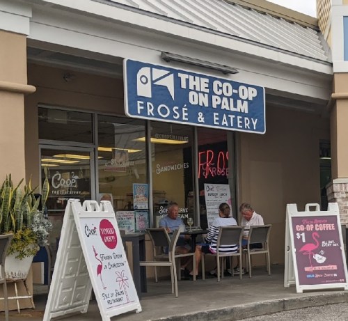 Exterior of The Co-Op on Palm, featuring a sign, outdoor seating, and sandwich specials displayed on signs.