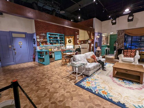 A cozy living room set with a sofa, coffee table, and kitchen area, featuring colorful decor and a warm atmosphere.