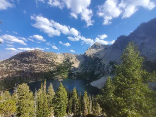 A scenic view of a mountain lake surrounded by trees and rocky peaks under a partly cloudy sky.
