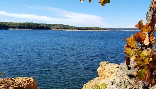 A serene lake surrounded by trees and rocky shores under a clear blue sky.