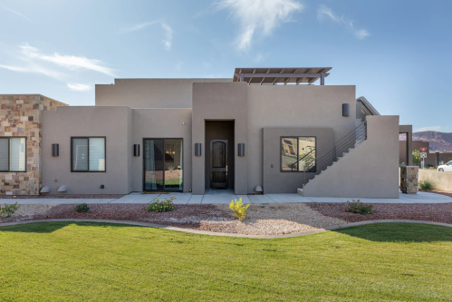 Modern beige house with a landscaped yard, featuring a staircase and large windows under a clear blue sky.