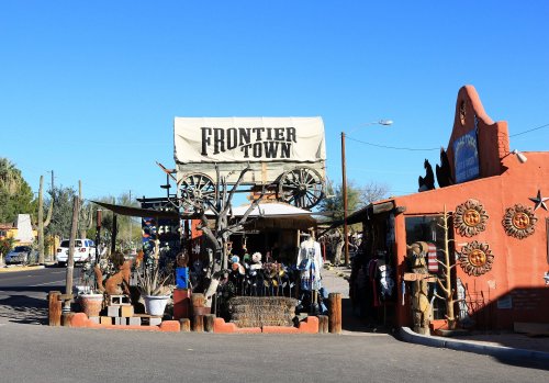 A western-themed storefront with a sign reading "Frontier Town" and a wagon on display under a clear blue sky.