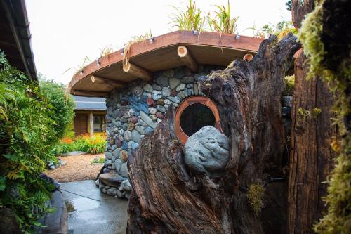 A unique stone and wood structure with a circular design, surrounded by lush greenery and a gravel pathway.