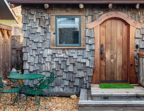 A rustic wooden cabin with a unique door, surrounded by a small patio and green chairs on a gravel path.