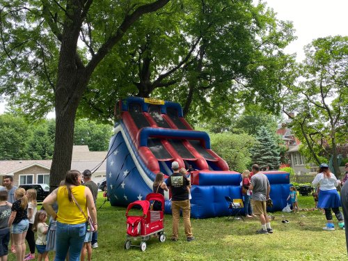 A large inflatable slide with red and blue colors, surrounded by children and adults in a grassy area.
