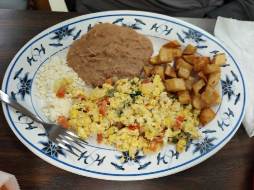 A plate of scrambled eggs with vegetables, refried beans, cheese, and crispy potato cubes on a decorative blue and white dish.