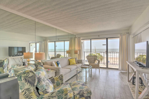 Bright beachside living room with large windows, white furniture, and tropical decor, overlooking the ocean.