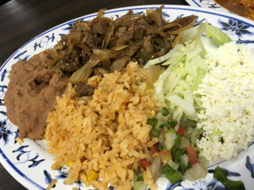 A colorful plate featuring rice, refried beans, sautéed beef with onions, lettuce, and crumbled cheese.