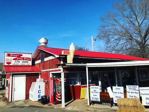 A red and white roadside diner with a sign for burgers and snacks, featuring an ice cream cone on the roof.