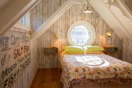 Cozy attic bedroom with a round window, wooden walls, and a colorful quilt on the bed. Soft lighting enhances the space.