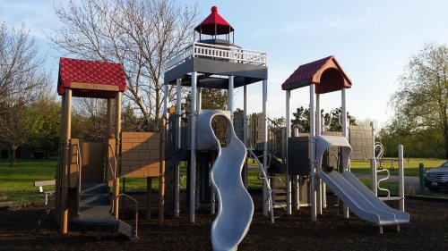 Colorful playground structure with slides and climbing areas, set in a grassy park under a clear blue sky.