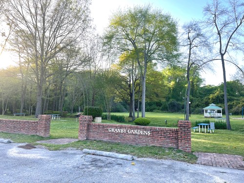 A brick sign reading "Granby Gardens" in a green park with trees and picnic tables in the background.