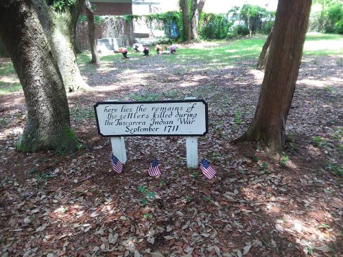 Sign marking the graves of settlers killed during the Tuscarora Indian War, surrounded by trees and small American flags.