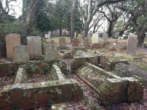 A historic cemetery with weathered gravestones and brick tombs, surrounded by trees and fallen leaves.