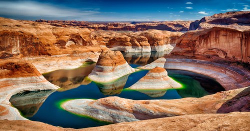 A stunning view of a canyon with red rock formations and a serene blue-green lake reflecting the sky.