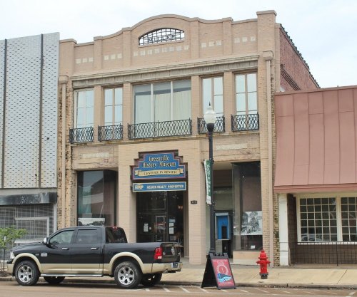Exterior of the Greenville History Museum, featuring a two-story building with large windows and a sign, parked truck in front.