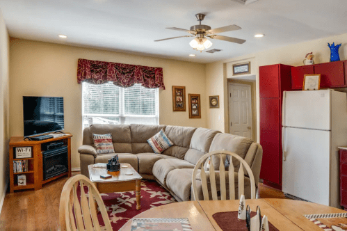 Cozy living room with a sectional sofa, TV, dining table, and red kitchen appliances in a bright, inviting space.