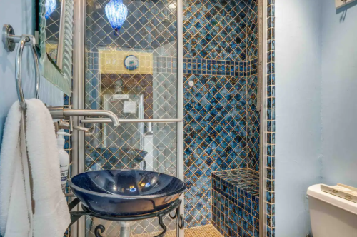A stylish bathroom featuring blue tiled walls, a glass shower, and a decorative sink.
