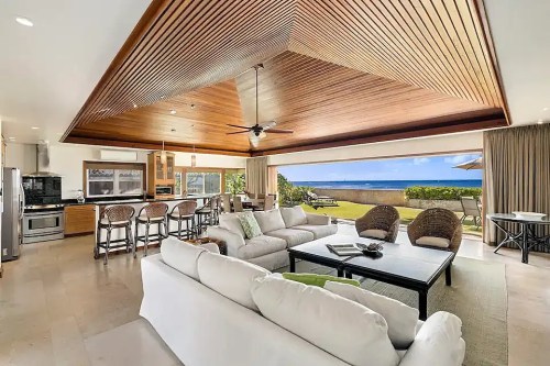 Bright, open living space with a wooden ceiling, modern kitchen, and ocean view through large sliding glass doors.