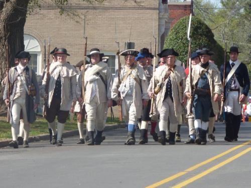 A group of men in historical military uniforms marching together on a street during a parade.
