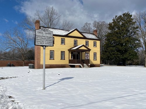 Historic Eagle Tavern, a yellow two-story building, surrounded by snow and trees under a blue sky with clouds.
