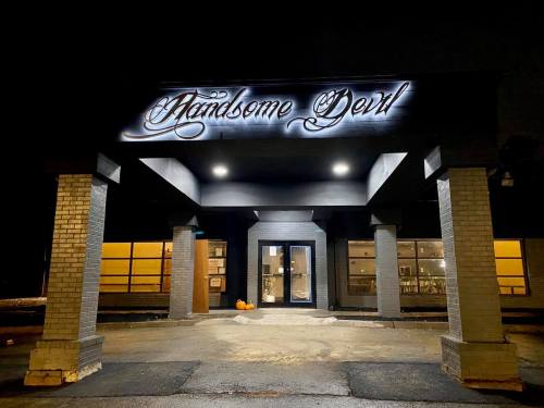 A dimly lit building at night with a sign reading "Handsome Devil" and a pumpkin on the ground.