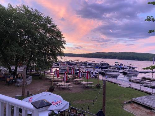 A serene lakeside view at sunset, featuring boats docked and outdoor seating with umbrellas.
