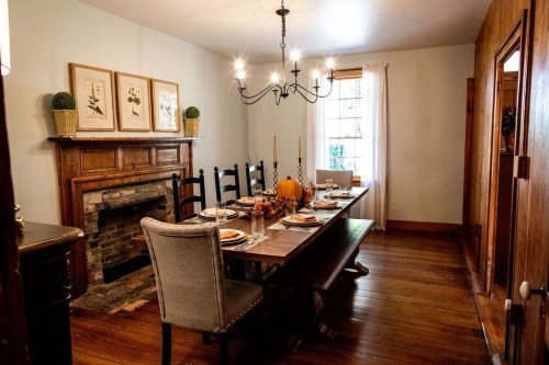 A cozy dining room with a long table set for a meal, featuring a chandelier and a fireplace.