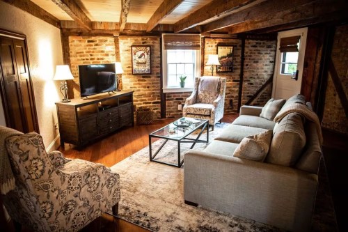 Cozy living room with exposed brick walls, wooden beams, a TV, and comfortable seating. Warm lighting enhances the ambiance.